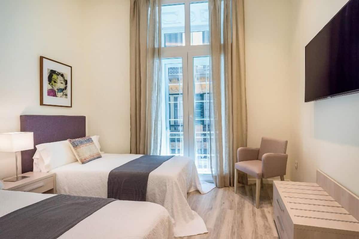 A hotel room with two beds, a TV, a chair, and a window with curtains.