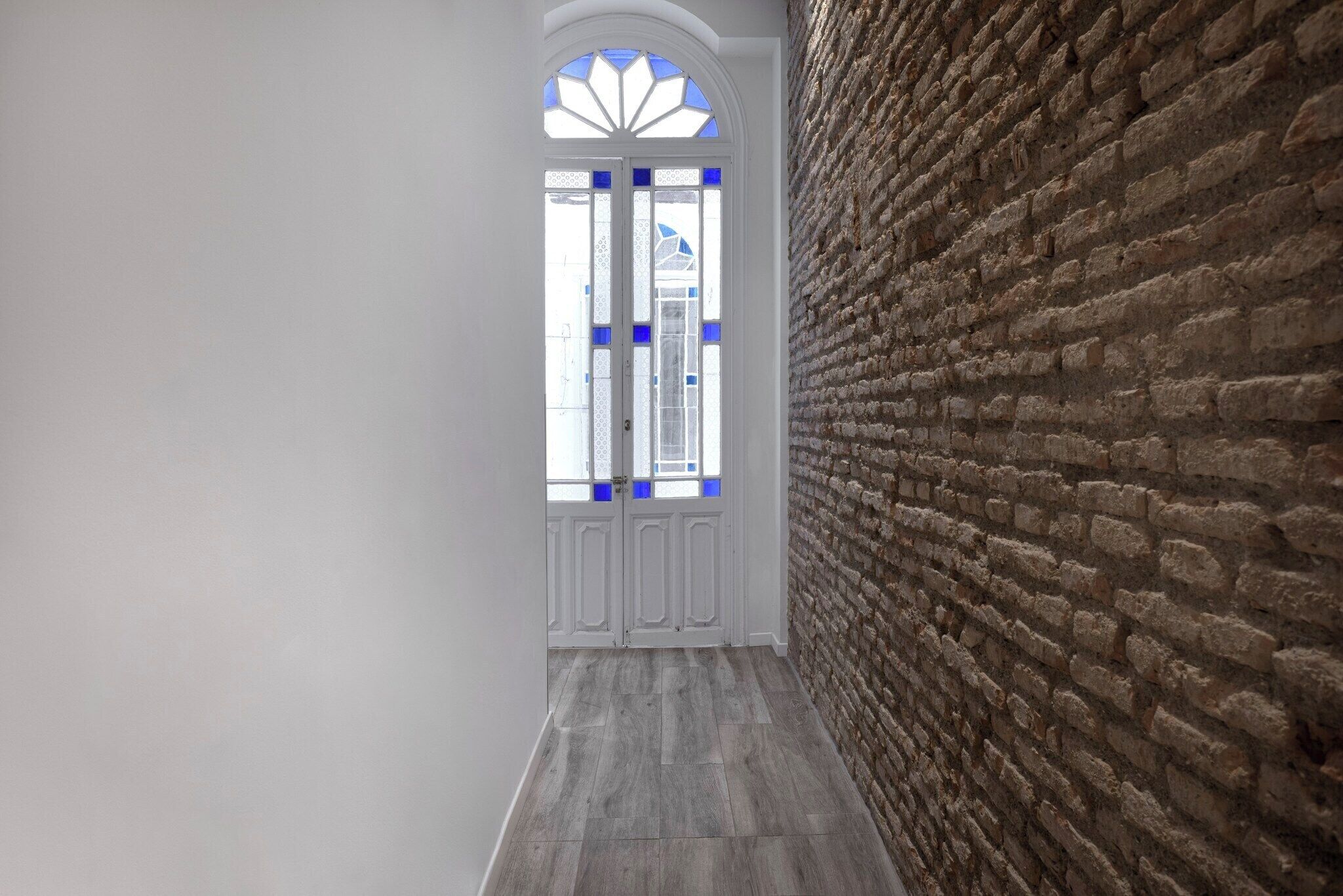 Un couloir avec un mur en briques et une porte blanche agrémentée de touches de bleu.