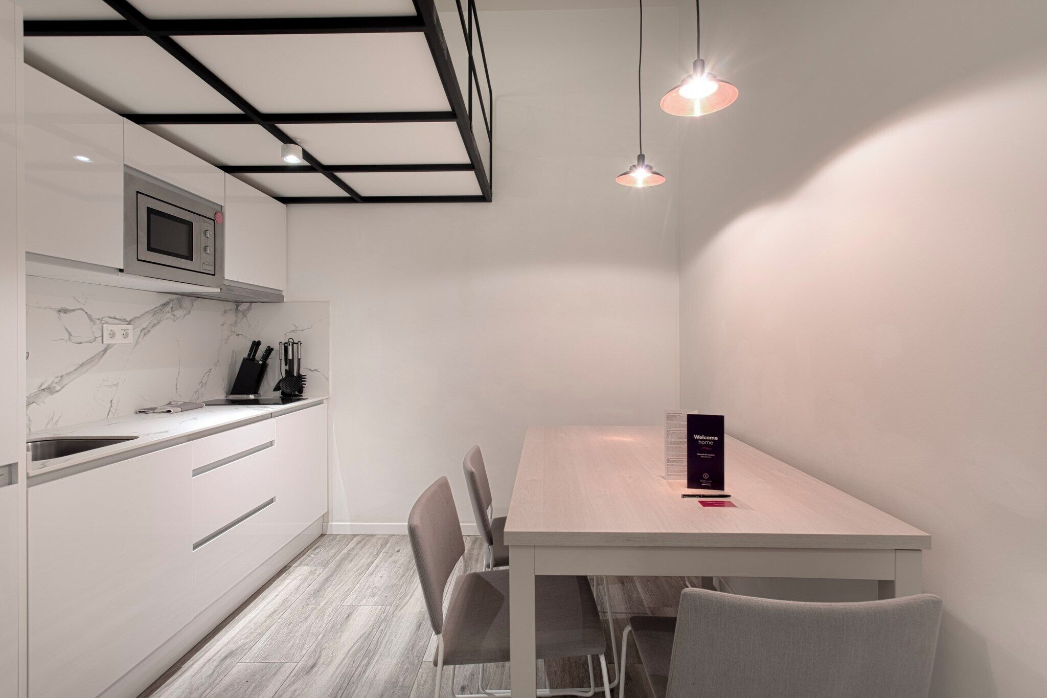 A modern kitchen with a built-in microwave, white cabinets, and a marble backsplash. There is a dining table with chairs and a menu stand.