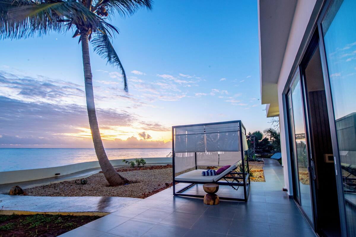 A modern outdoor seating area with a view of the ocean at sunset.