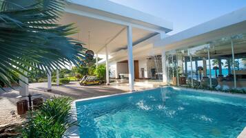 Ein moderner Poolbereich mit einem klaren blauen Pool, weißen Säulen und einem überdachten Lounge-Bereich aus Glas.