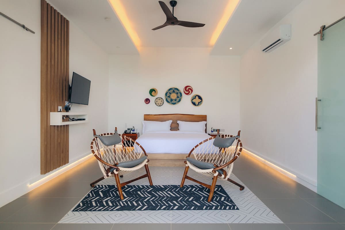 A modern hotel room with a bed, two wicker chairs, a TV, decorative plates, and a ceiling fan.