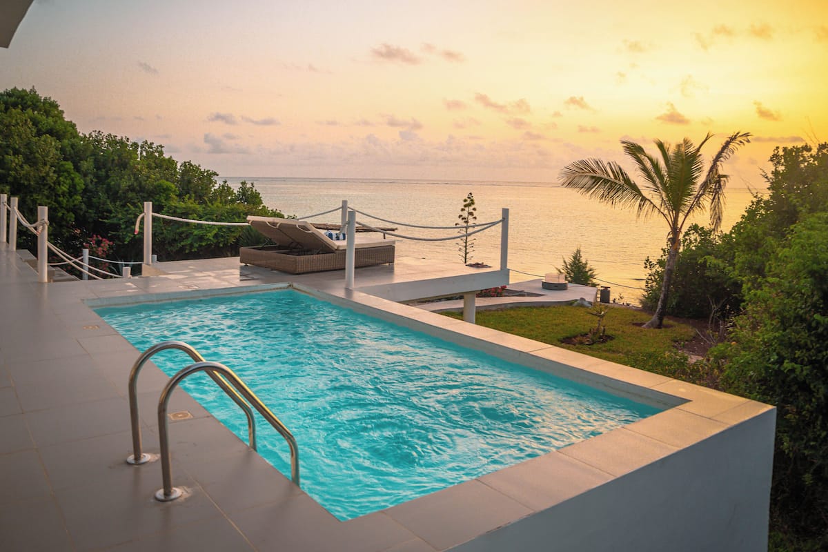 A rectangular pool with a metal ladder, surrounded by a white deck and a rope barrier.