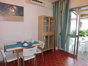 Uma sala de jantar com mesa, cadeiras, um armário e vista através de uma porta de vidro.