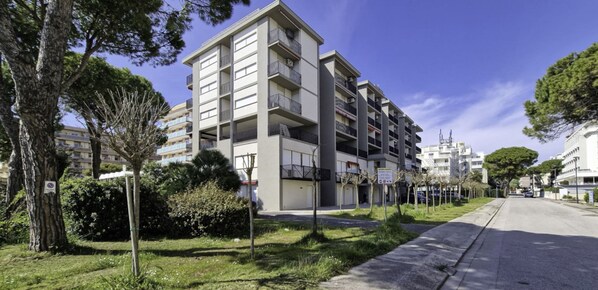 A multi-story residential building with balconies, surrounded by trees and a clear sky.
