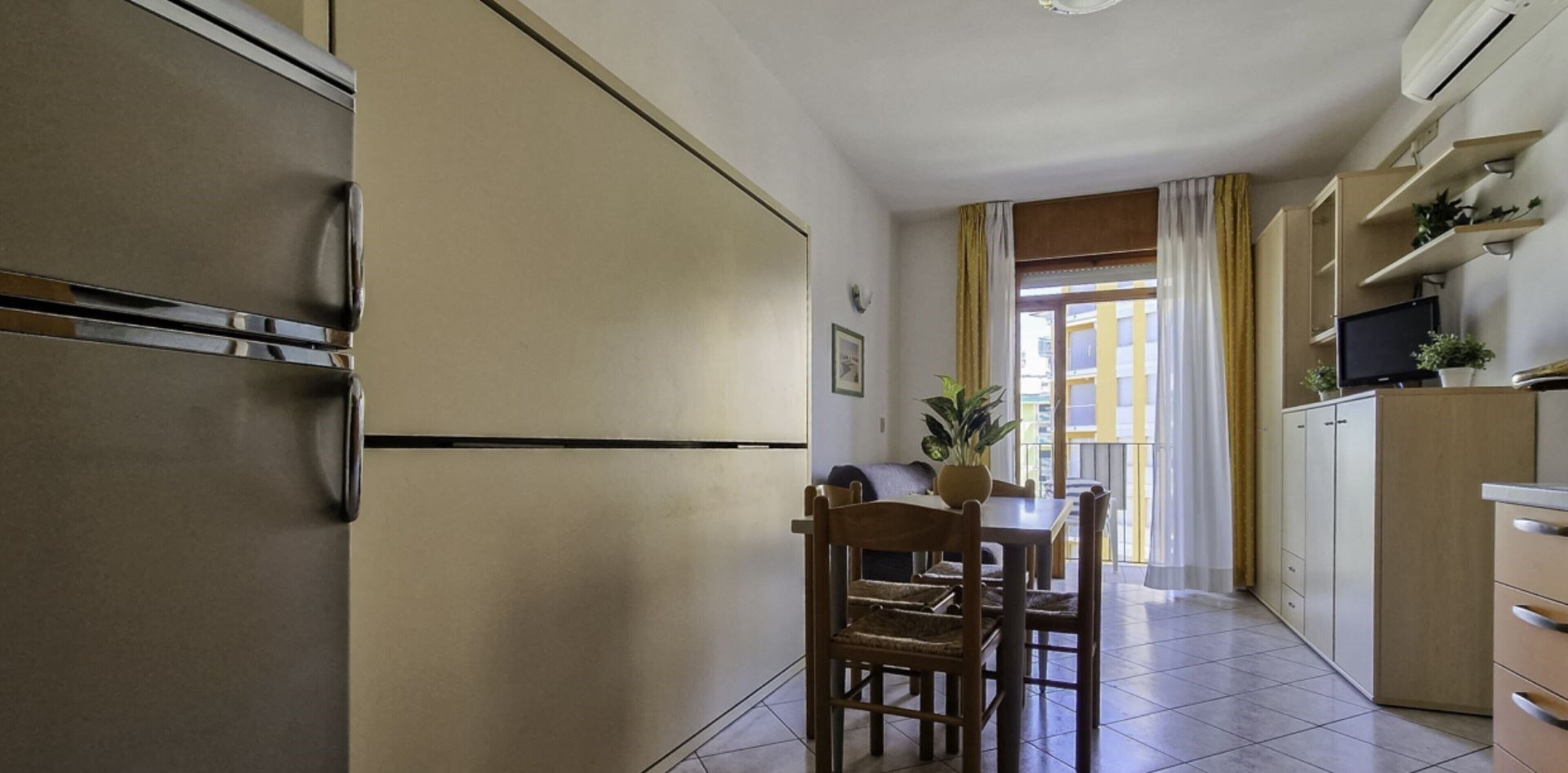 A compact kitchen with a refrigerator, a dining table with chairs, and a TV on a cabinet.