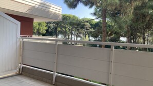 A balcony with a white railing, a tiled floor, and a view of trees and a building in the background.
