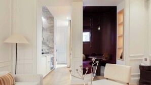 A modern living room with a sofa, a coffee table, and a lamp. There is a dining area with a table and chairs in the background. - The Lander - Serviced 1BR/1BA - Louvre-Rivoli III (Paris)