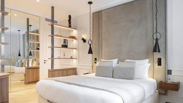 A modern bedroom with a large bed, built-in shelving, and pendant lighting. - The Lander - Serviced 1BR/1BA - Louvre-Rivoli III (Paris)