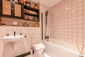 A bathroom with a sink, toilet, and bathtub, featuring a grid-patterned wall and shelves with toiletries. - Stylish Hackney Wick Home (London)