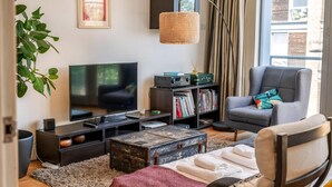Un salon comprenant un téléviseur, une bibliothèque, un fauteuil et une grande fenêtre.