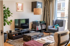 A living room with a television, bookshelf, armchair, and a large window. - Bright & Spacious Battersea Flat (London)