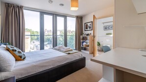 Une chambre d’hôtel moderne dotée d’un grand lit, d’un bureau et offrant une vue sur la ville grâce à de grandes fenêtres.