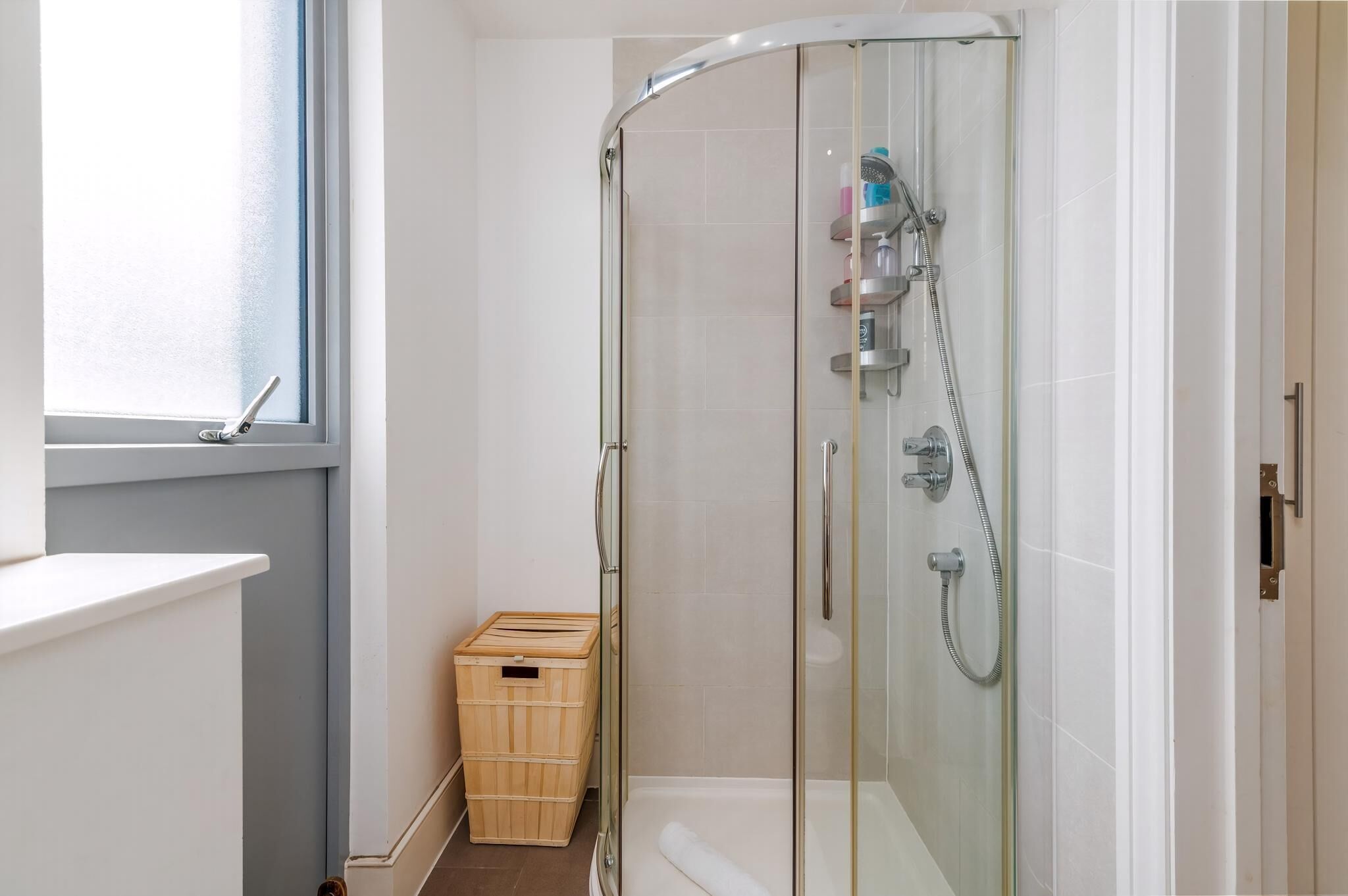 A glass-enclosed shower with a handheld showerhead and a handheld faucet.