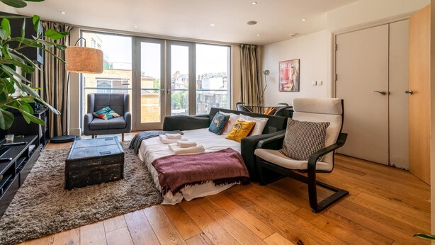 Un salon moderne avec un canapé, un fauteuil et une petite table. Il y a une grande fenêtre avec des rideaux, une plante et une affiche accrochée au mur.