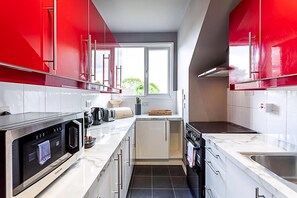 A modern kitchen with red cabinets, a built-in oven, and a large window. - Stylish Cosy Apartment (London)