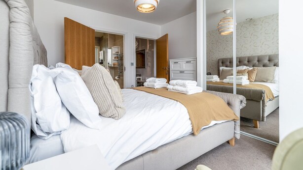 Une chambre d’hôtel moderne dotée d’un grand lit, d’une armoire, d’une salle de bain et d’un miroir qui reflète la pièce.