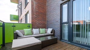 Un espace extérieur moderne, aménagé avec un canapé et une table à plateau en verre, un meuble vert et une terrasse en bois.