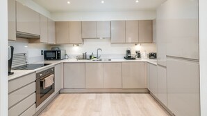 Une cuisine moderne avec des meubles de couleur bois clair, un four encastré, un four à micro-ondes, une machine à café et un évier.