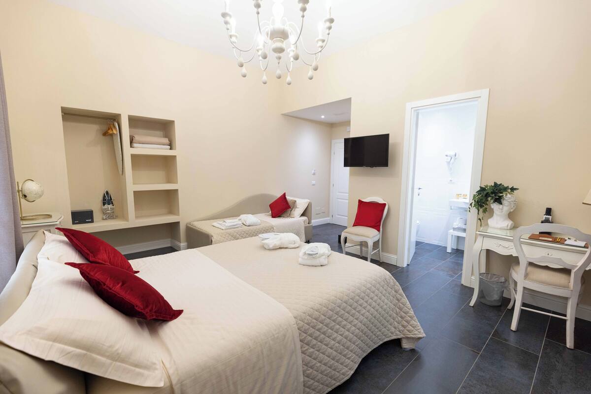 A hotel room with a large bed, a desk, a chair, a TV mounted on the wall, and a small plant.