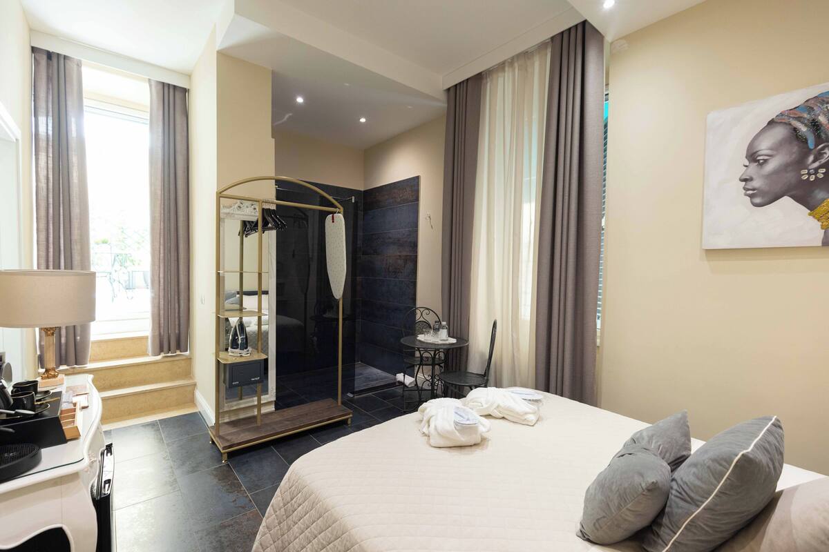 A hotel room with a large bed, a sitting area with a table and chairs, a mirror, and a shower area.