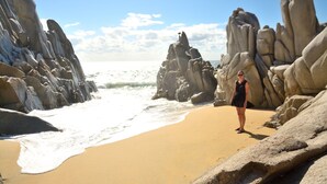 A beach with large rock formations and a person standing on the sand. - Cabo Oasis Escape - 1 Bedroom Apartment (Cabo San Lucas)