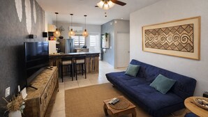 A living room with a sofa, TV, and a kitchen area with a bar. - Cabo Oasis Escape - 1 Bedroom Apartment (Cabo San Lucas)