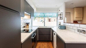A modern kitchen with a central island, built-in appliances, and a large window providing natural light. - Terraced Bermondsey House (London)