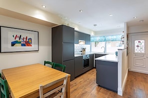 A modern kitchen with dark cabinets, a wooden dining table, and a tiled backsplash. - Terraced Bermondsey House (London)