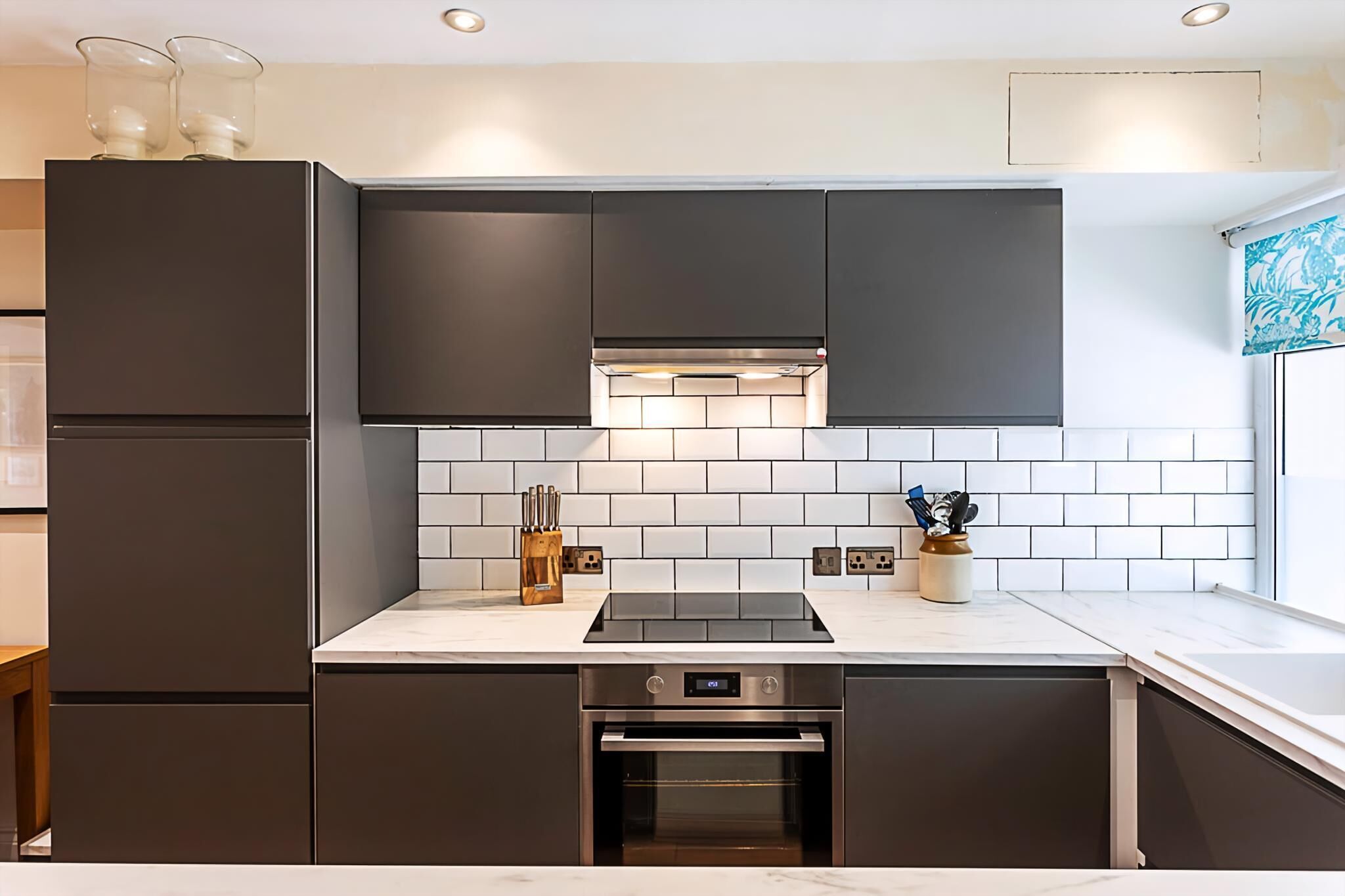 A modern kitchen with dark cabinets, a white tiled backsplash, and a stainless steel oven.