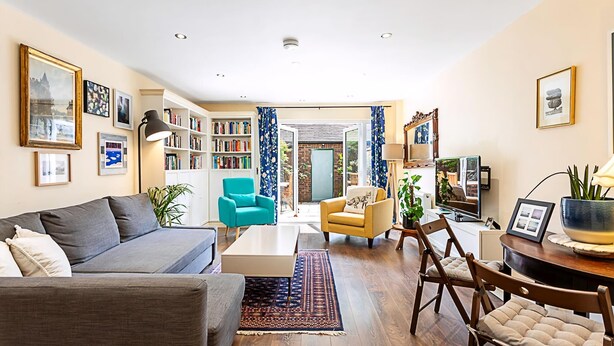 A living room with a sofa, armchairs, a coffee table, a bookshelf, and a dining area with chairs. - Terraced Bermondsey House (London)