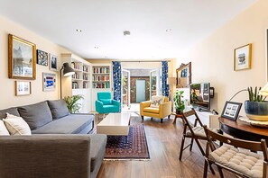 A living room with a sofa, armchairs, a coffee table, a bookshelf, and a dining area with chairs.