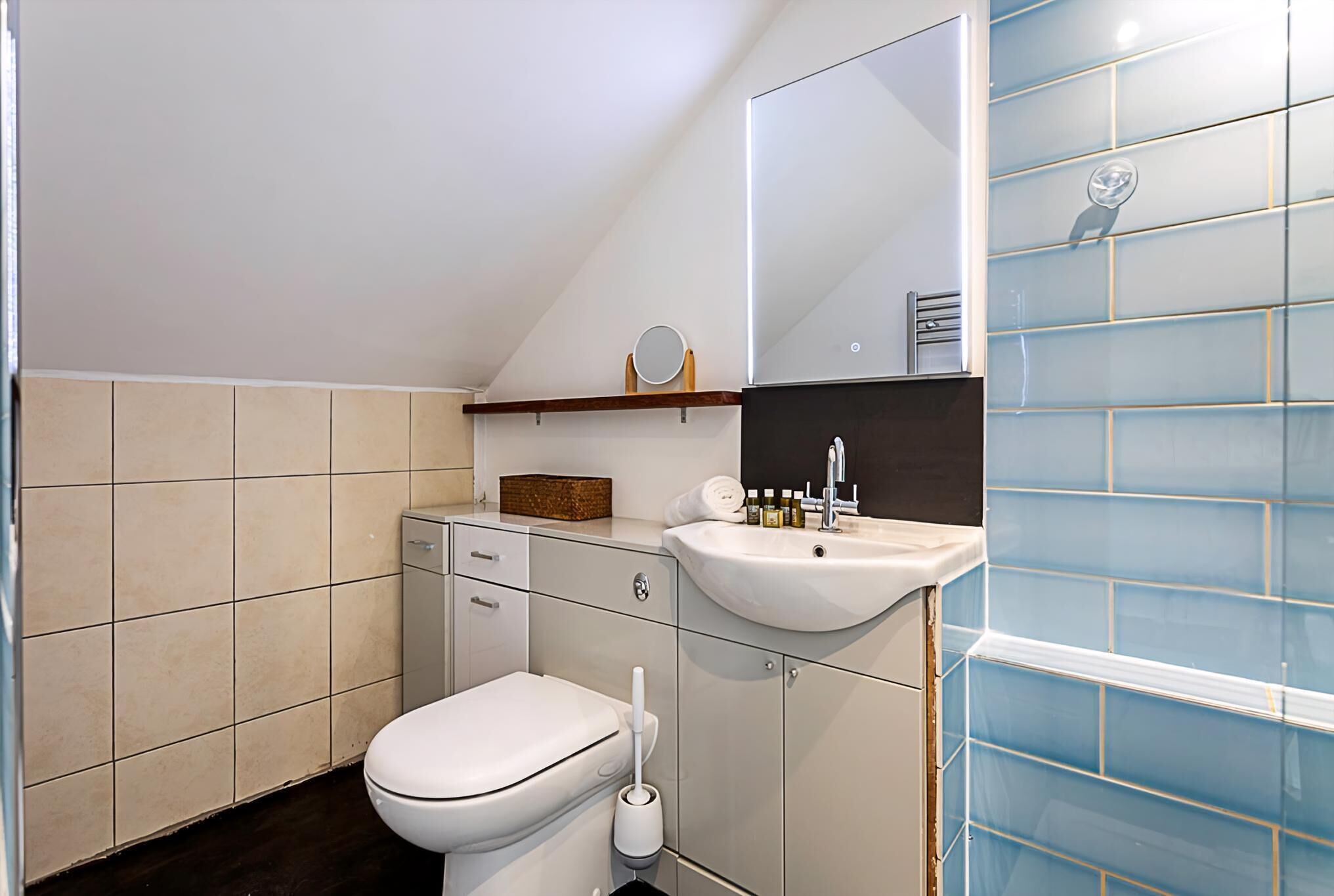 Ein modernes Badezimmer mit Toilette, Waschbecken, Spiegel und blauen Fliesen.