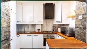 Una cocina compacta con armarios blancos, una encimera de madera, una estufa a gas, un microondas y un horno empotrado.