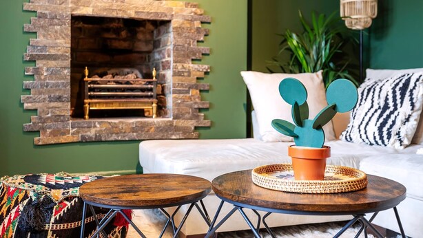 Una sala de estar acogedora con una chimenea de piedra, un sofá blanco y dos mesitas de madera redondas.