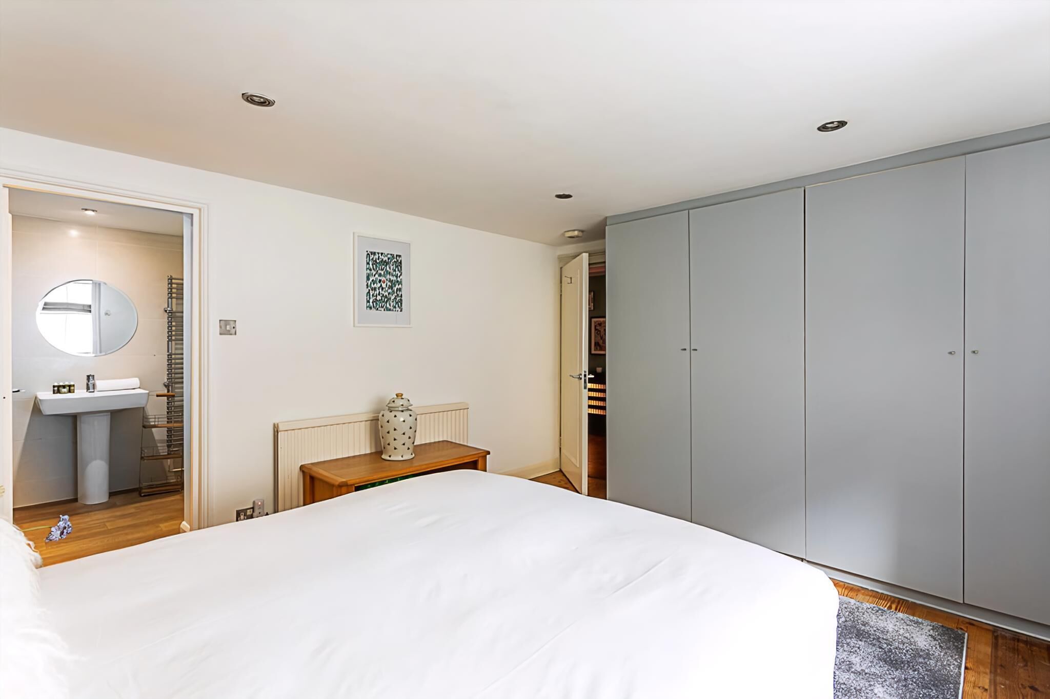 A bedroom with a bed, a wardrobe, a bedside table, a mirror, and a radiator.