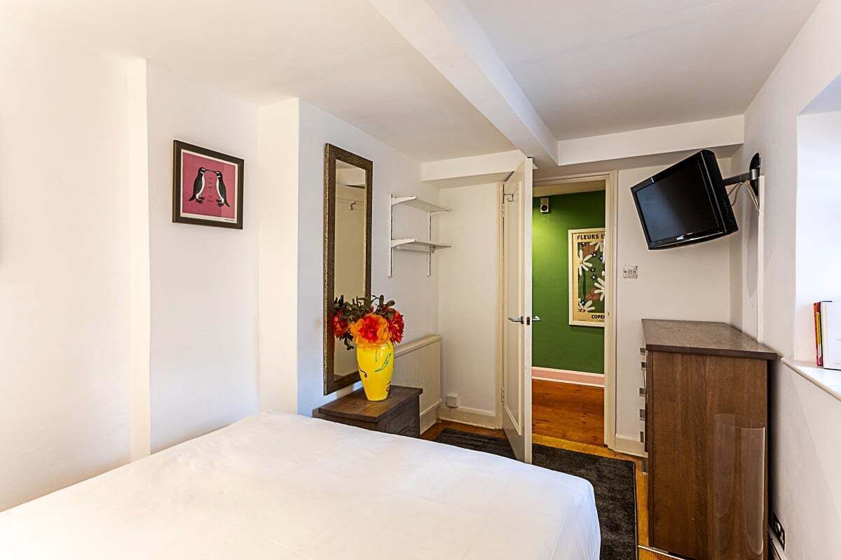 A hotel room with a bed, a mirror, a TV mounted on the wall, and a small cabinet.