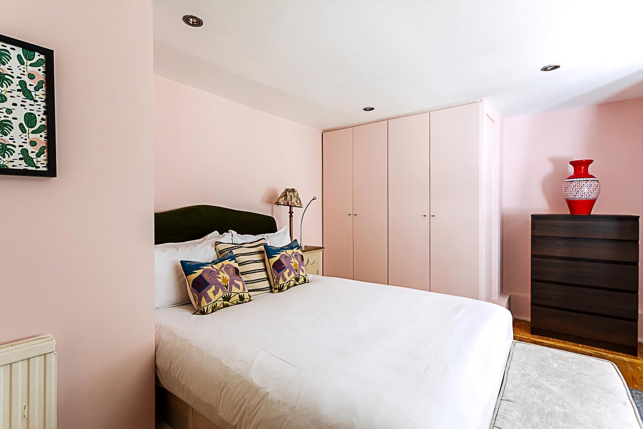 Un dormitorio con cama, almohadas, una mesita de noche, lámpara, armario y cómoda.