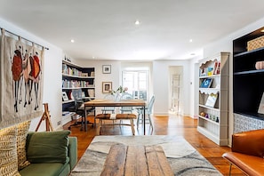 A spacious living room with a wooden dining table, a green sofa, and a bookshelf filled with books. - Cottage Style Three Bedroom House (London)