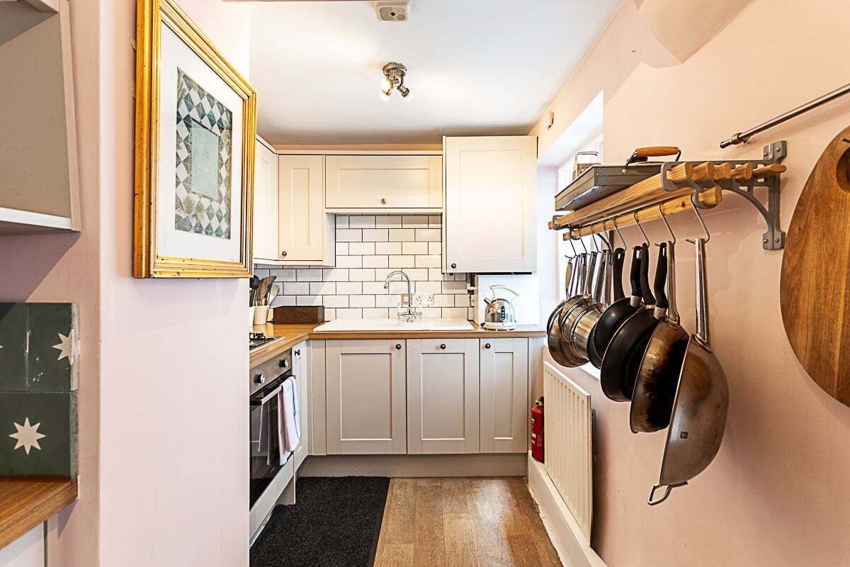 A narrow kitchen with white cabinets, a black rug, and a pot rack.