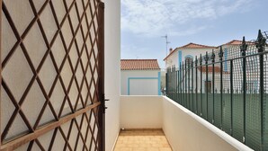 A narrow balcony with a metal gate, a tiled floor, and a view of a building with a red-tiled roof and blue trim.