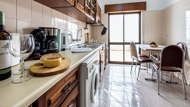 A kitchen with wooden cabinets, a coffee maker, a wine glass, and a dining area with chairs and a table.