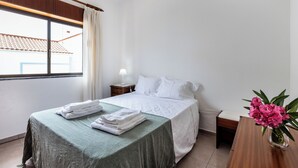 A hotel room with a bed, a nightstand, a lamp, a window with curtains, and a vase with flowers.