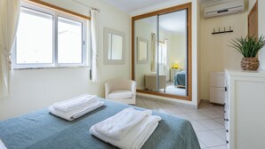 Un dormitorio con cama, una silla, un aparador, un espejo y una planta en maceta.
