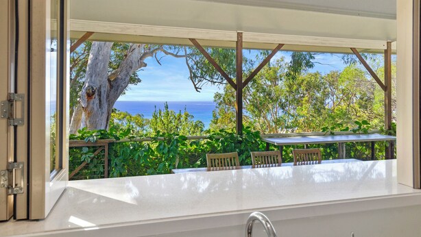 Ein überdachter Außenbereich mit Blick auf das Meer, ein Tisch und Stühle.
