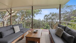 Ein überdachter Außenbereich mit zwei grauen Sofas, einem Holztisch und Blick auf Bäume und Himmel.