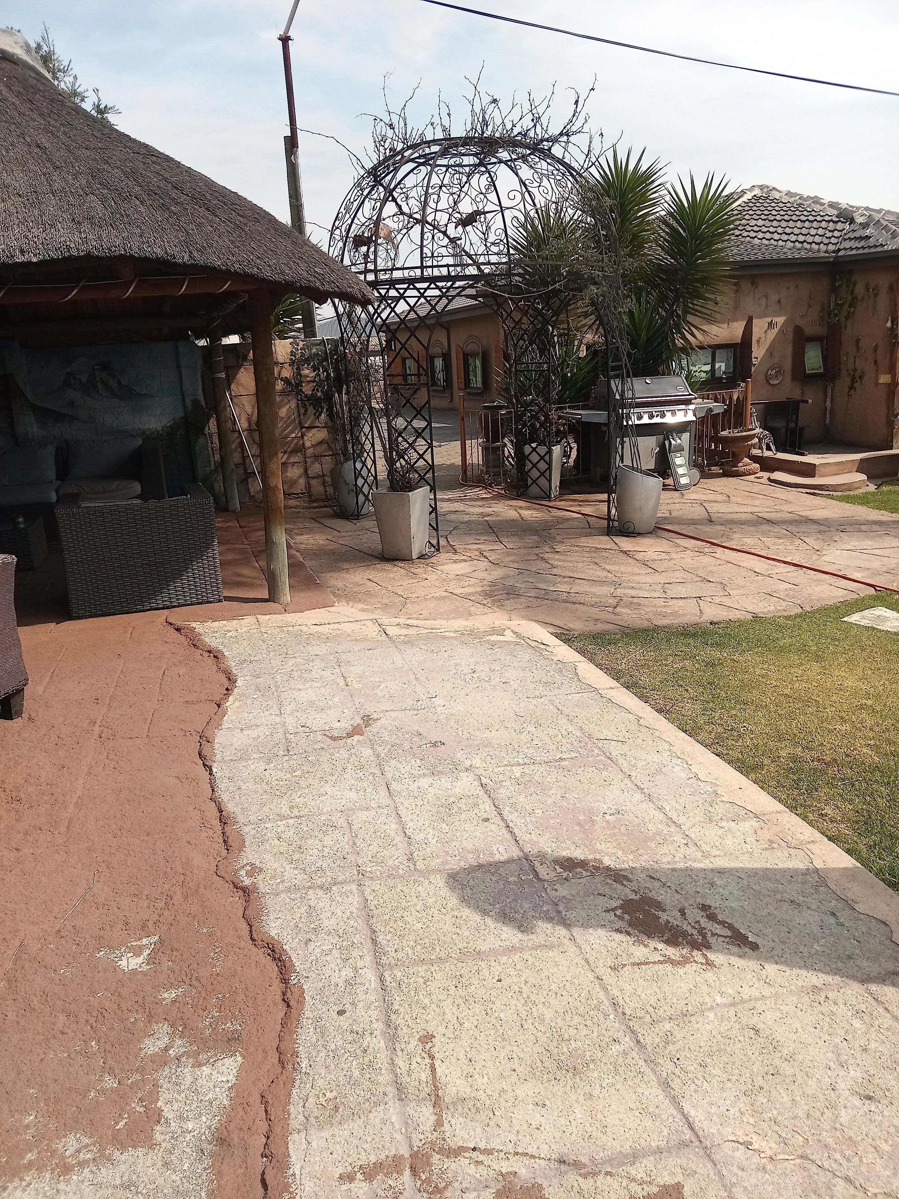 Um pátio com uma construção de telhado de palha, um portão de metal e área para churrasco.