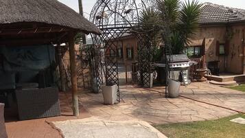 Um pátio com uma construção de telhado de palha, um portão de metal e área para churrasco.