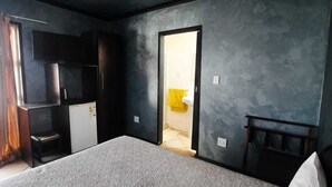 Een slaapkamer met een bed, een televisie, een kledingkast en een badkamer zichtbaar door een geopende deur.