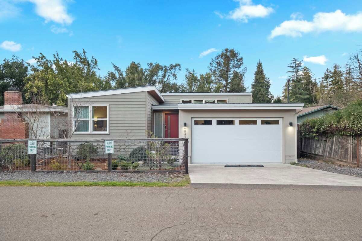 A modern two-story house with a garage, a fenced yard, and a clear sky.
